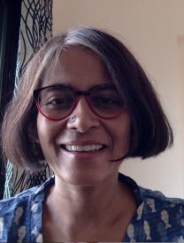 Photo of Lalitha with red and black rimmed glasses and a blue blouse. 